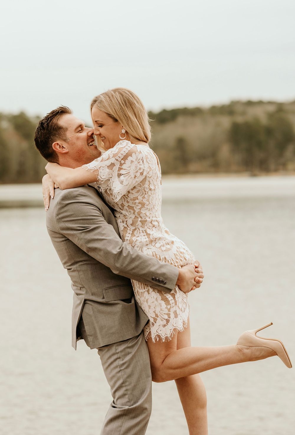 A joyful couple embracing in formal wear against a waterfront backdrop.