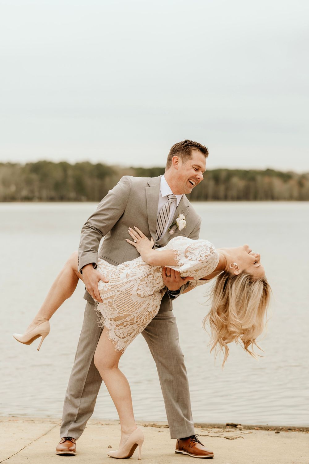 A playful dip pose between a couple in formal wear by the water.