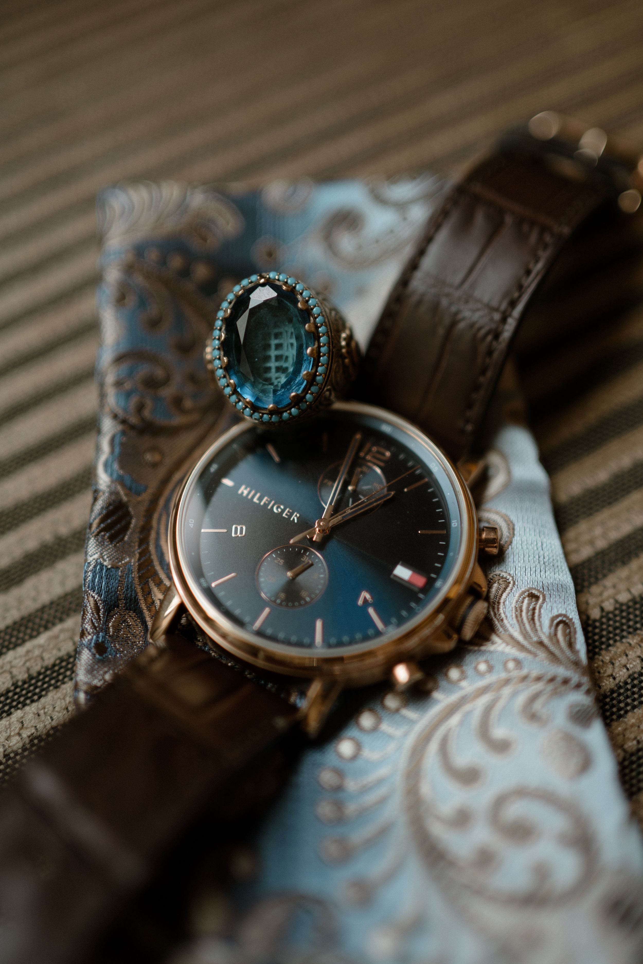 Elegant wristwatch with blue face and leather strap displayed on decorative fabric.