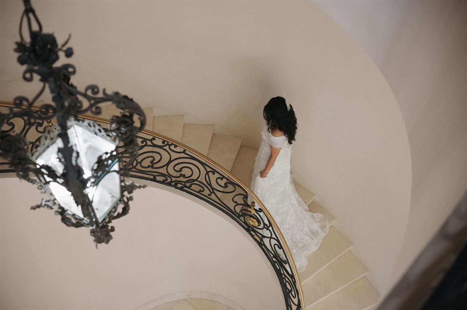An ornate vintage chandelier hangs above a spiral staircase where a bride descends.