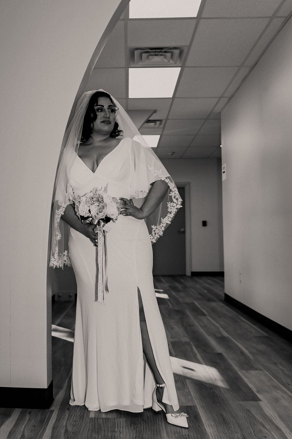 A person wearing a white dress stands in an indoor hallway with hardwood floors.