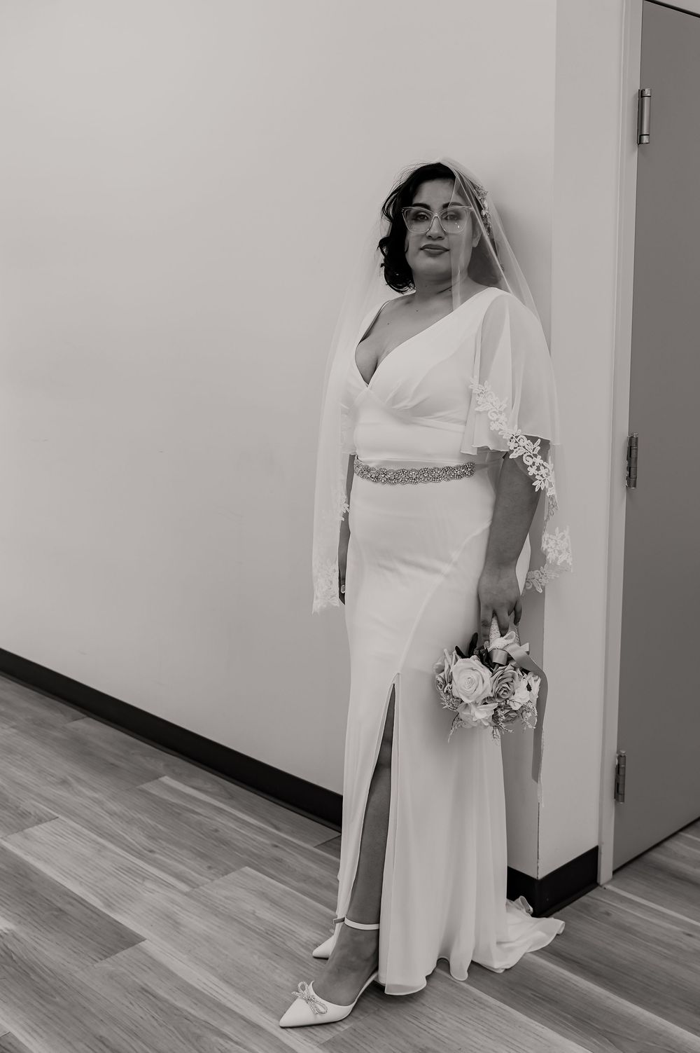 A bride in a white dress poses in a hallway with natural lighting.