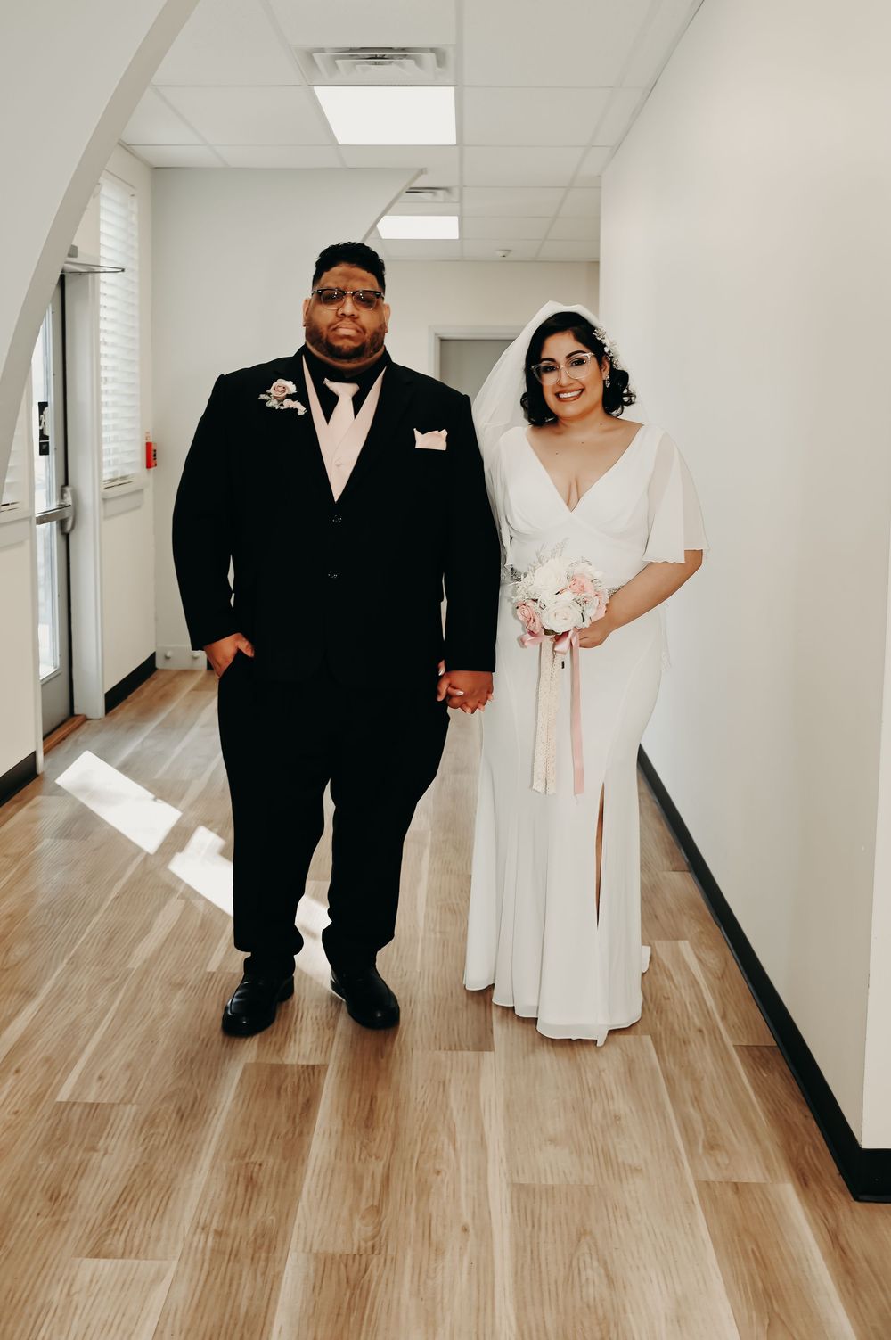 Couple walking down a bright hallway with wooden floors during their wedding day.