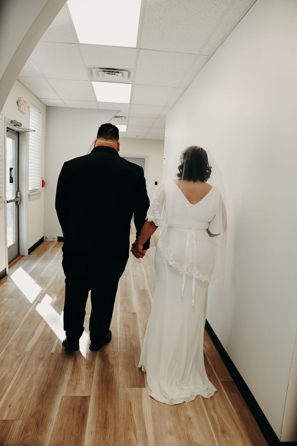 Wedding couple walking down a bright hallway after their ceremony.