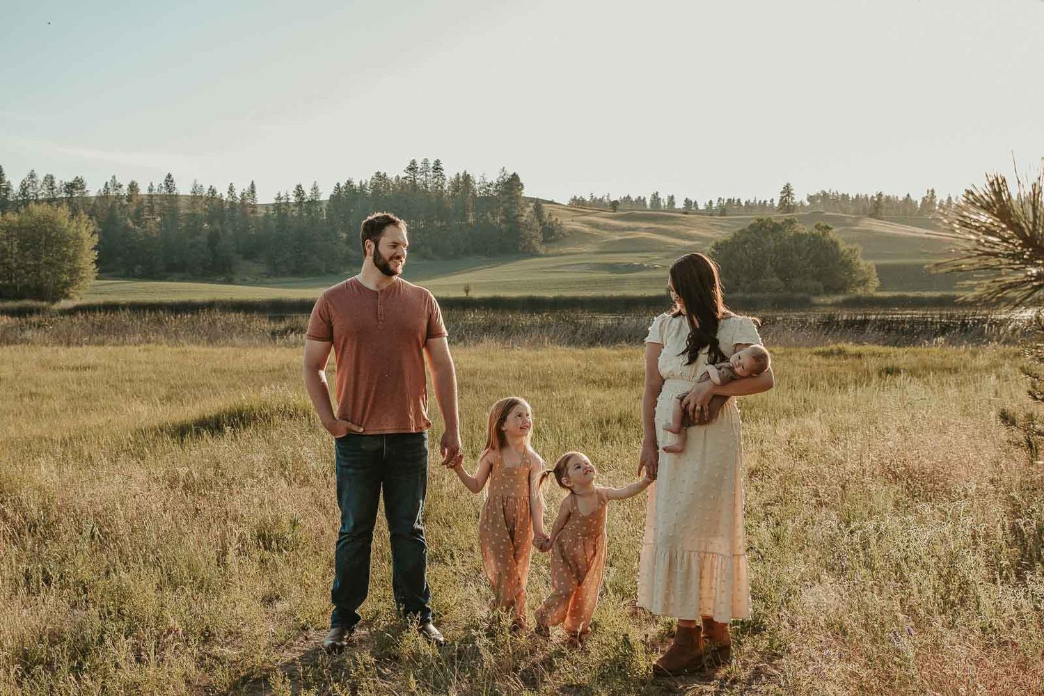 Family of 5 in earth tone outfits at sunset in open field with hills, lake in background at Spokane outdoor photo venue