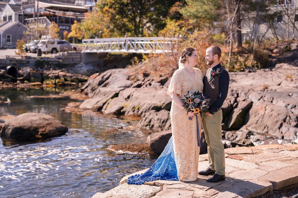 A couple sits together on large rocks by a scenic waterfront on an autumn afternoon.