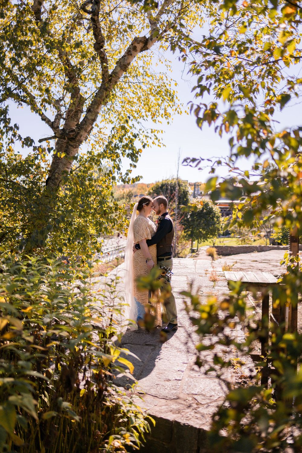 A couple shares an intimate moment on a sunny autumn day surrounded by golden leaves and natural light.