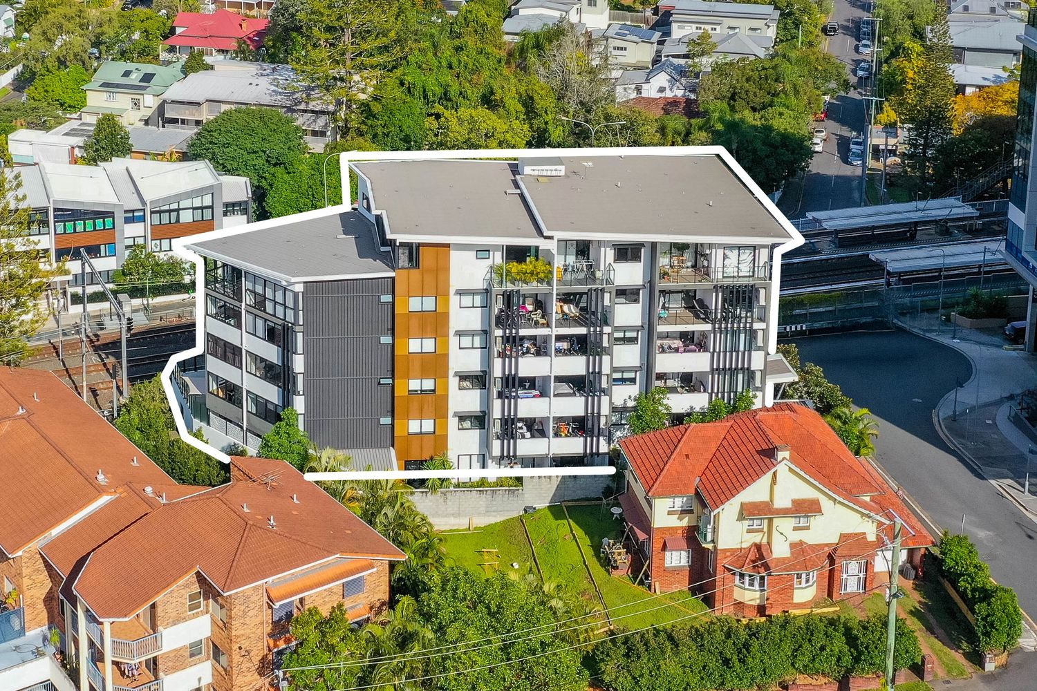 Aerial view of a modern multi-storey apartment building surrounded by lush trees in an urban Brisbane suburb.