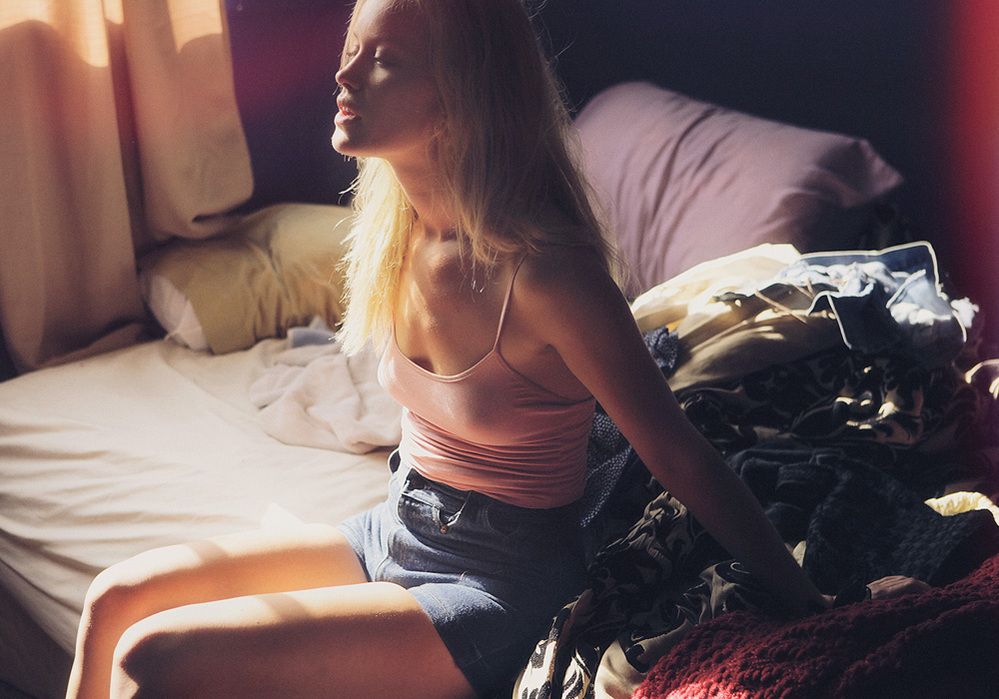 Moody atmospheric bedroom scene with pink top and denim shorts in warm sunlight through window.