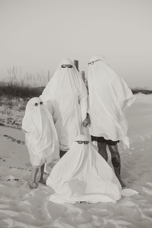 Artistic black and white photos of ghostly figures in white sheets standing on a sandy beach.
