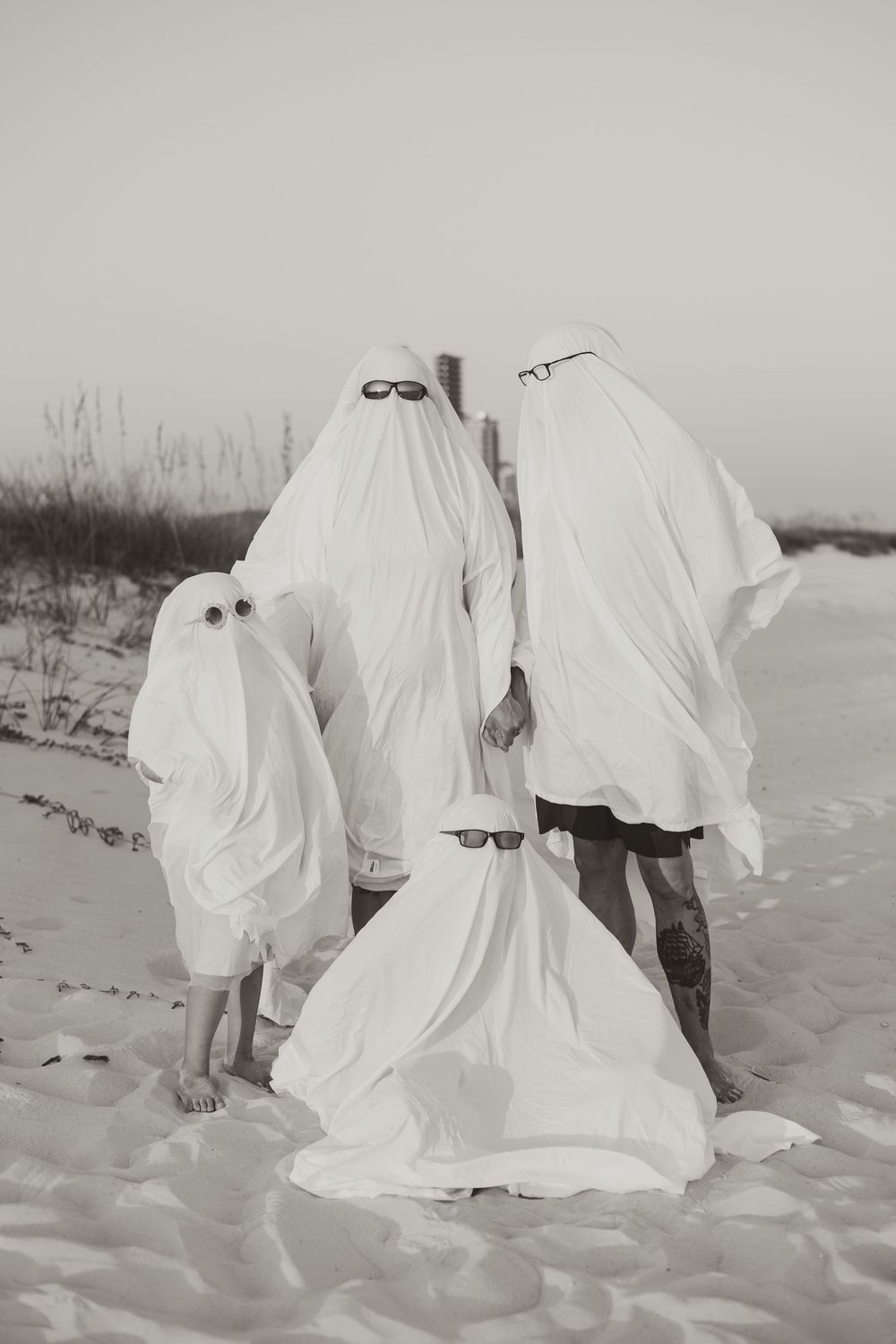 Artistic black and white photos of ghostly figures in white sheets standing on a sandy beach.