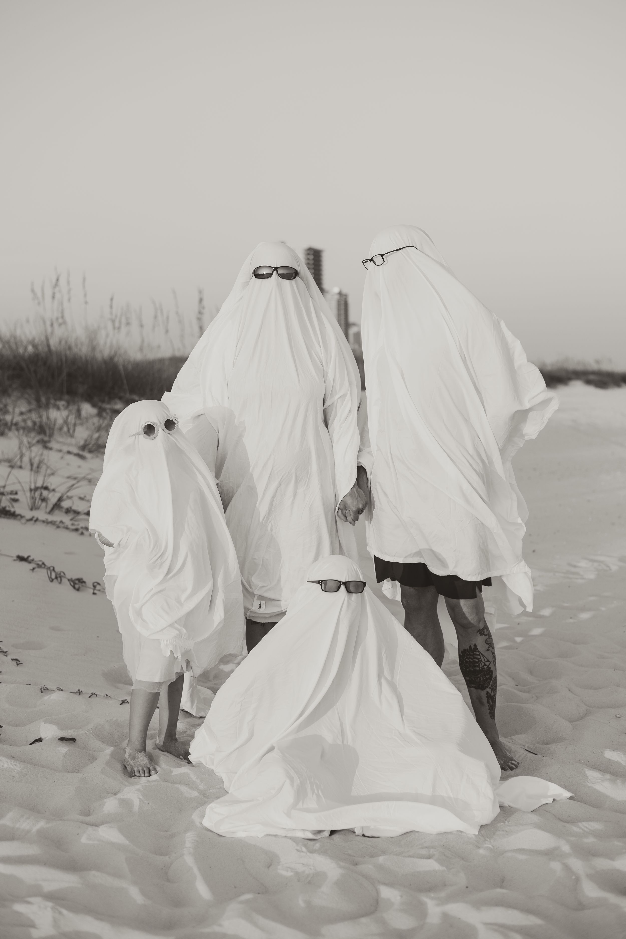 Artistic black and white photos of ghostly figures in white sheets standing on a sandy beach.