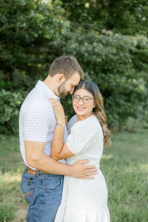 Couple in casual white outfits embrace in outdoor garden setting.