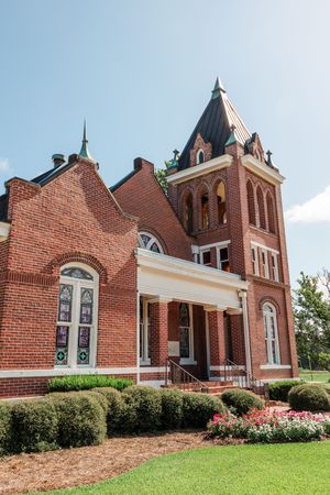 Historic red brick church with gothic architecture and stained glass windows under blue sky.