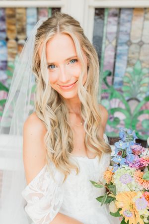 A bride in a white wedding dress holds a colorful bouquet of spring flowers.