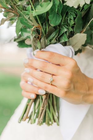Close-up of hands holding a fresh green bouquet with engagement ring prominently displayed.