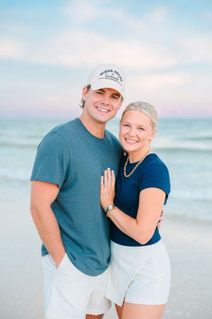 A couple poses together on a beach at sunset wearing coordinating navy blue and white outfits.
