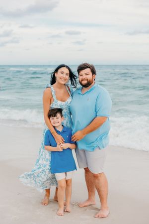 Family wearing coordinating blue outfits poses together on a sunny beach.