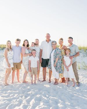 Large family group portrait on white sand beach, smiling multi-generational family in coordinated outfits on sunny day.