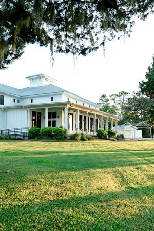White Southern plantation-style event venue with wraparound porch, columns, and lush green lawn surrounded by Spanish moss trees.