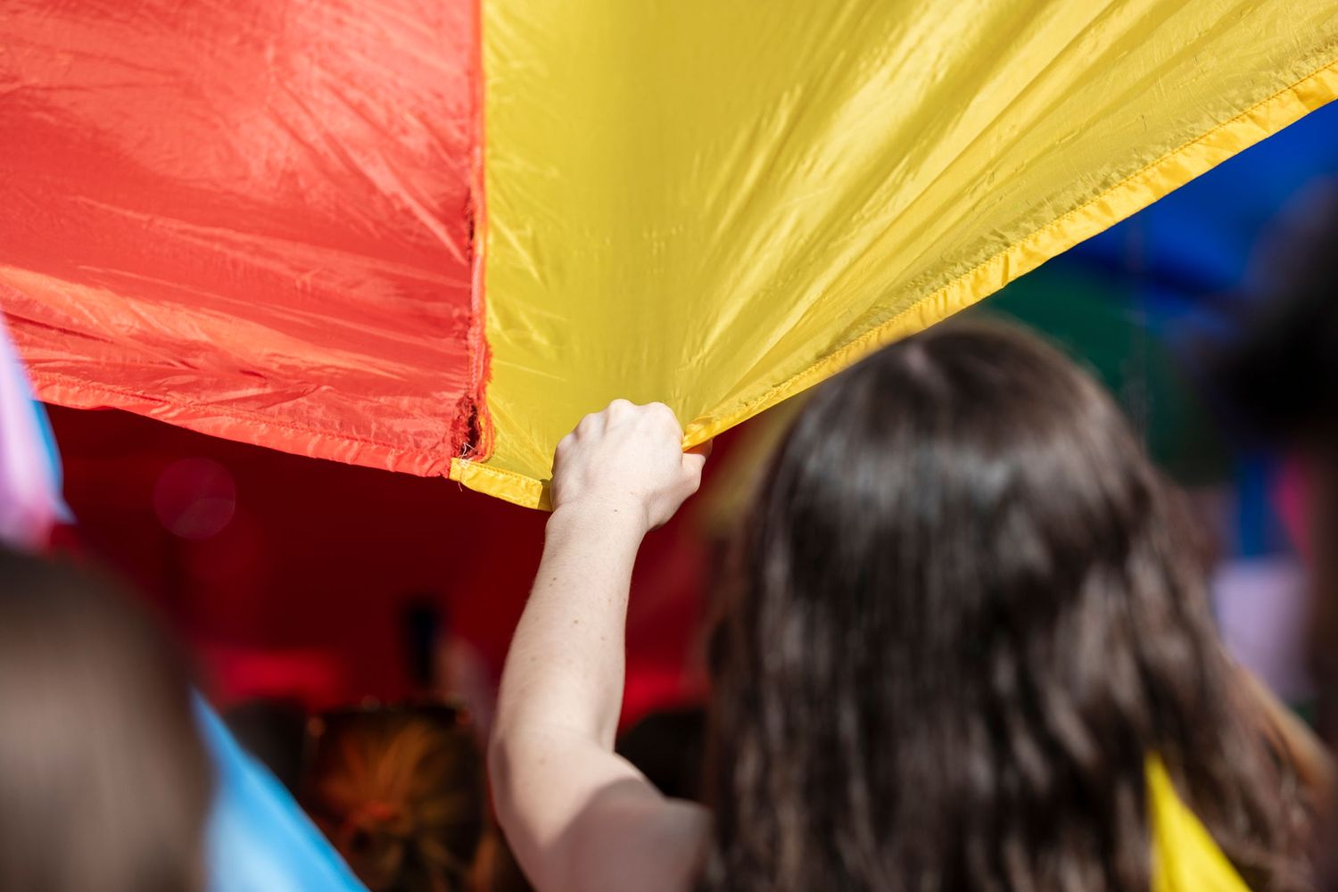 Someone holds up a colorful red and yellow banner during a pride celebration or parade event.