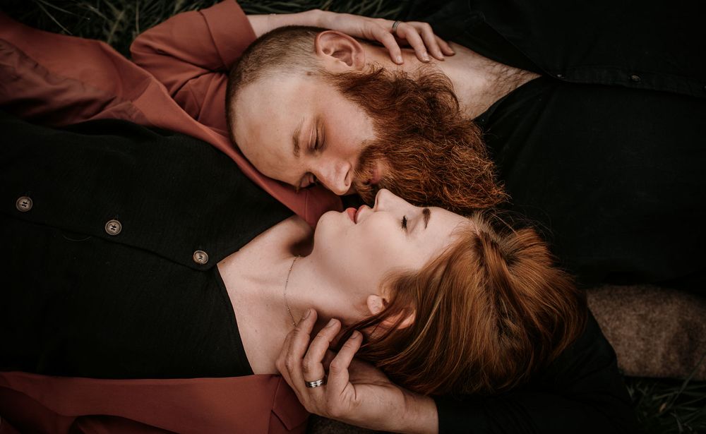 Overhead view of couple lying in grass, nearly kissing, with hands gently touching.