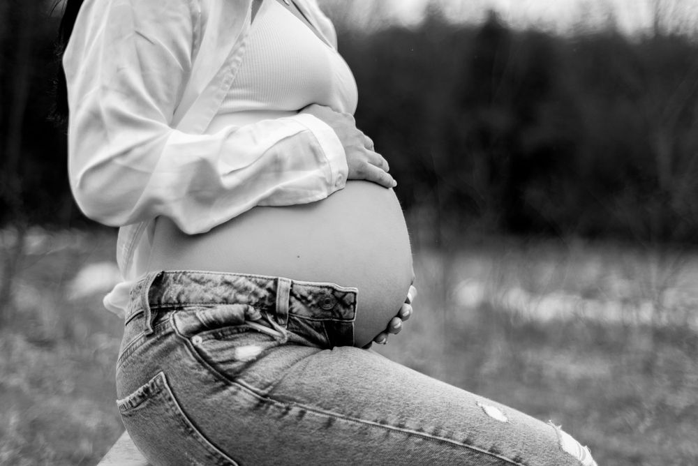 Black and white side view of a pregnant belly in casual jeans and white top.