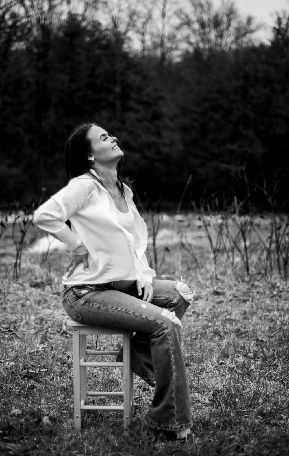 Black and white portrait of person seated on wooden chair in outdoor field.