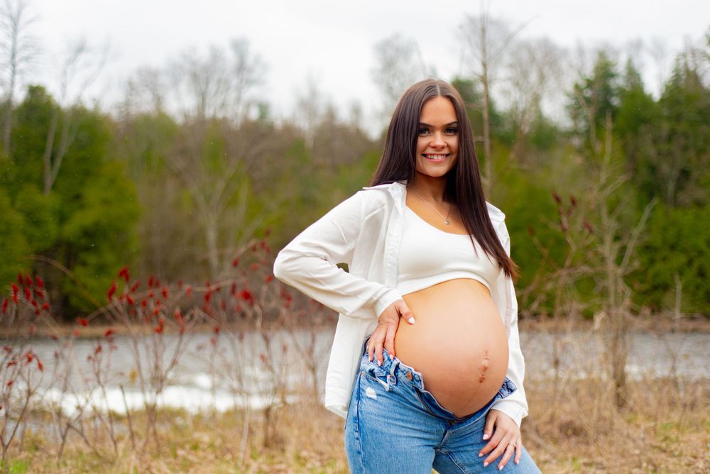Outdoor pregnancy photo with person wearing white shirt and jeans showing baby bump.