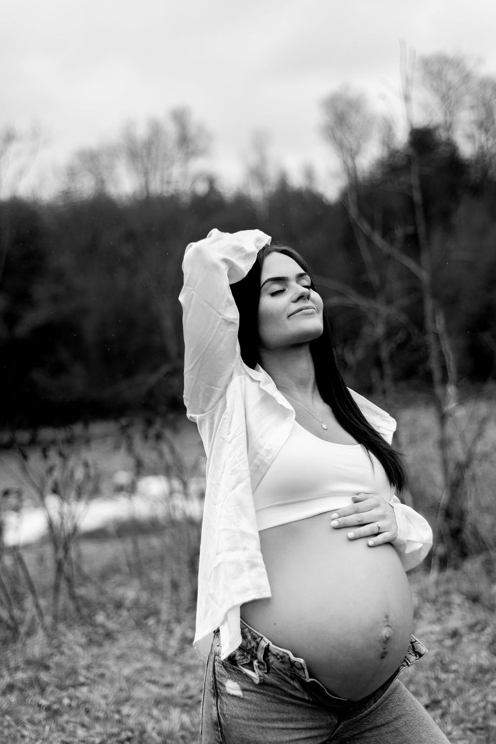 Black and white maternity photo showing pregnant belly against natural outdoor background.