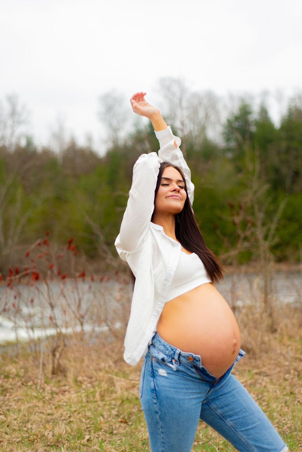 Joyful maternity pose with arms raised showing pregnant belly in outdoor setting.