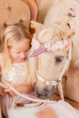 Child interacting with a pony wearing pink floral accessories at a party.