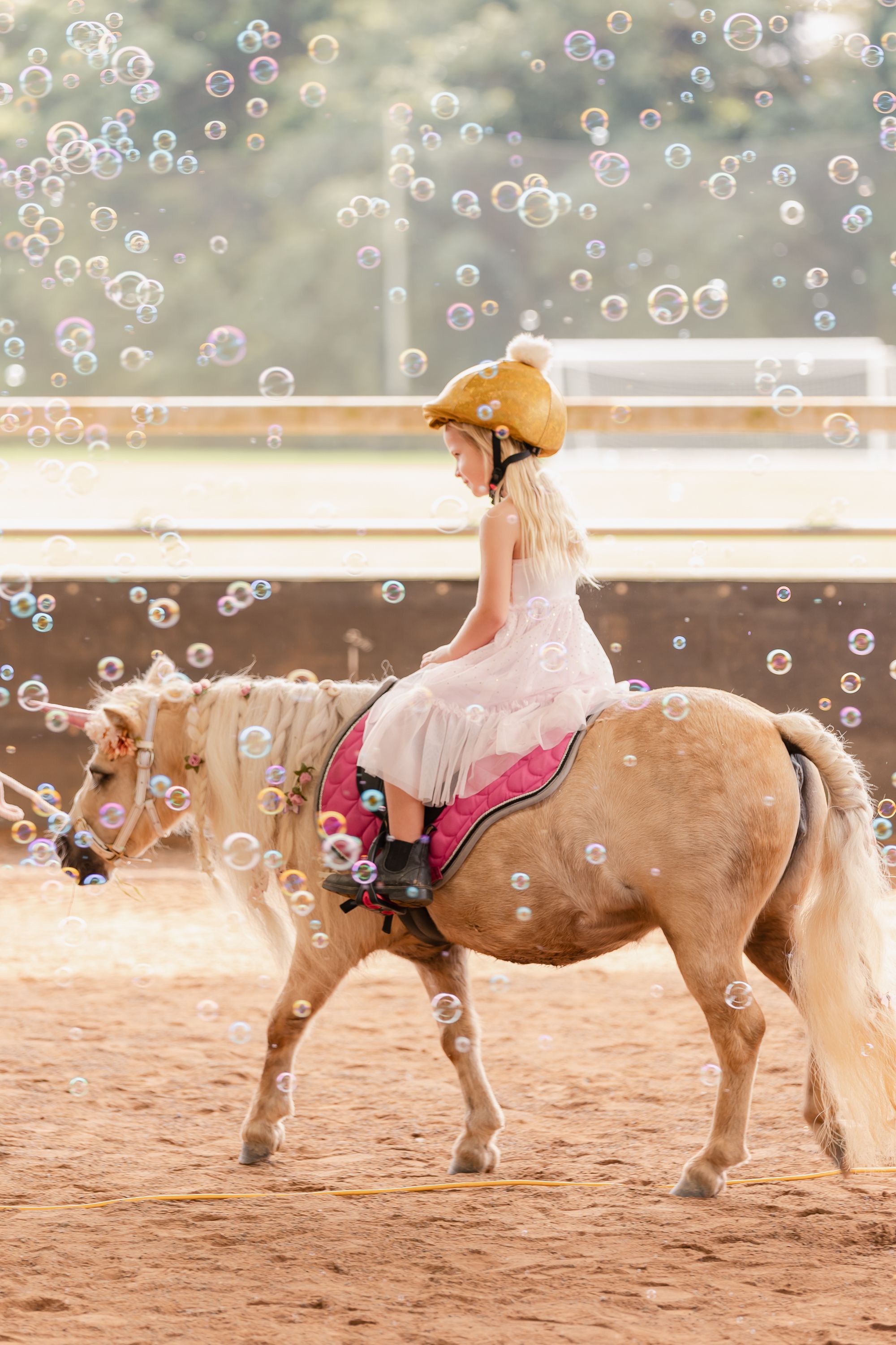 Pony ride under floating bubbles in a sandy arena during a special event.