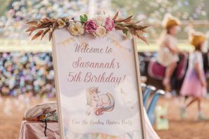 Delicate pink and white welcome signs with floral decorations at a birthday party celebration.