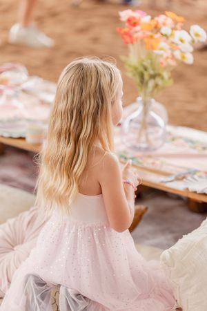 Children in light colored dresses seated at a decorated party table.