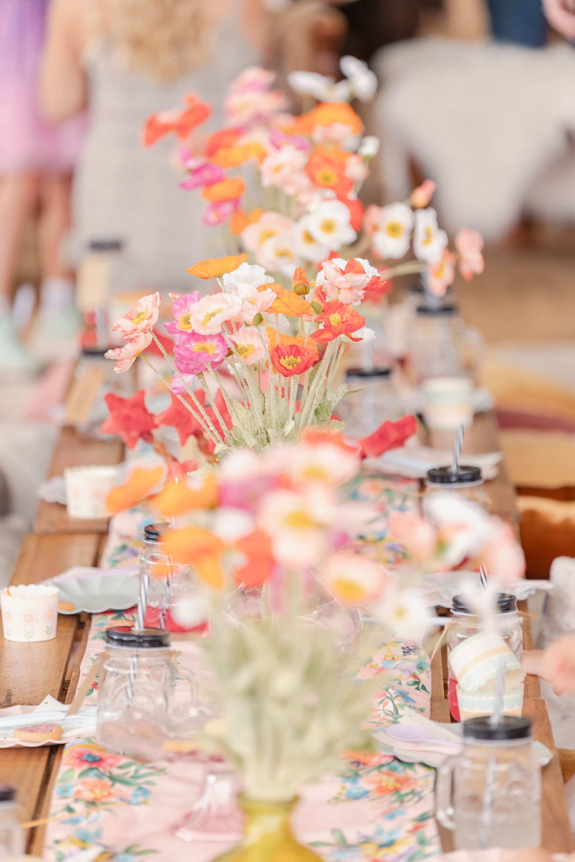 Party table setting with coral and pink flowers, glassware, and elegant place settings.