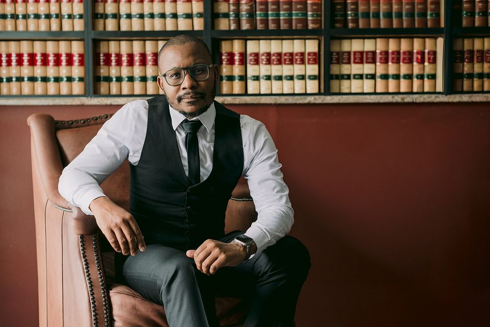 Professional man in vest and tie sits confidently in leather chair before law library bookshelves.