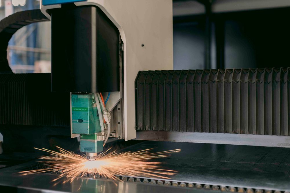 CNC laser cutting machine producing bright orange sparks while precision cutting a metal sheet in a factory.