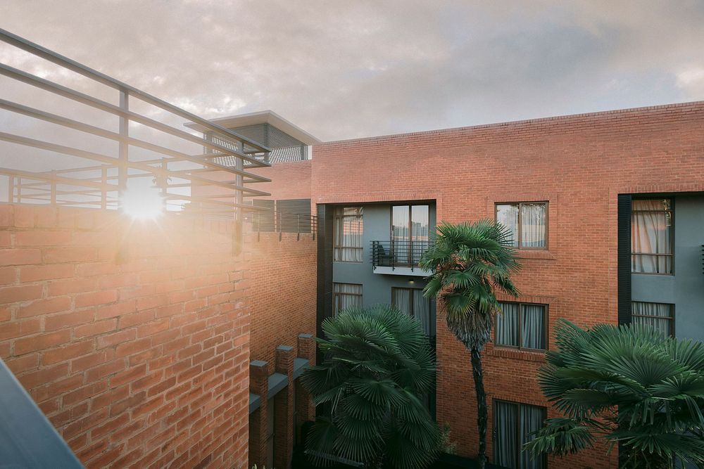 Brick hotel building exterior with palm trees, balconies, and warm sunlight glowing through at golden hour.