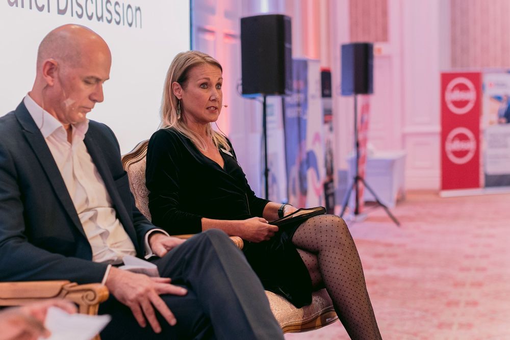 Man and woman seated on stage during a panel discussion at a corporate event.
