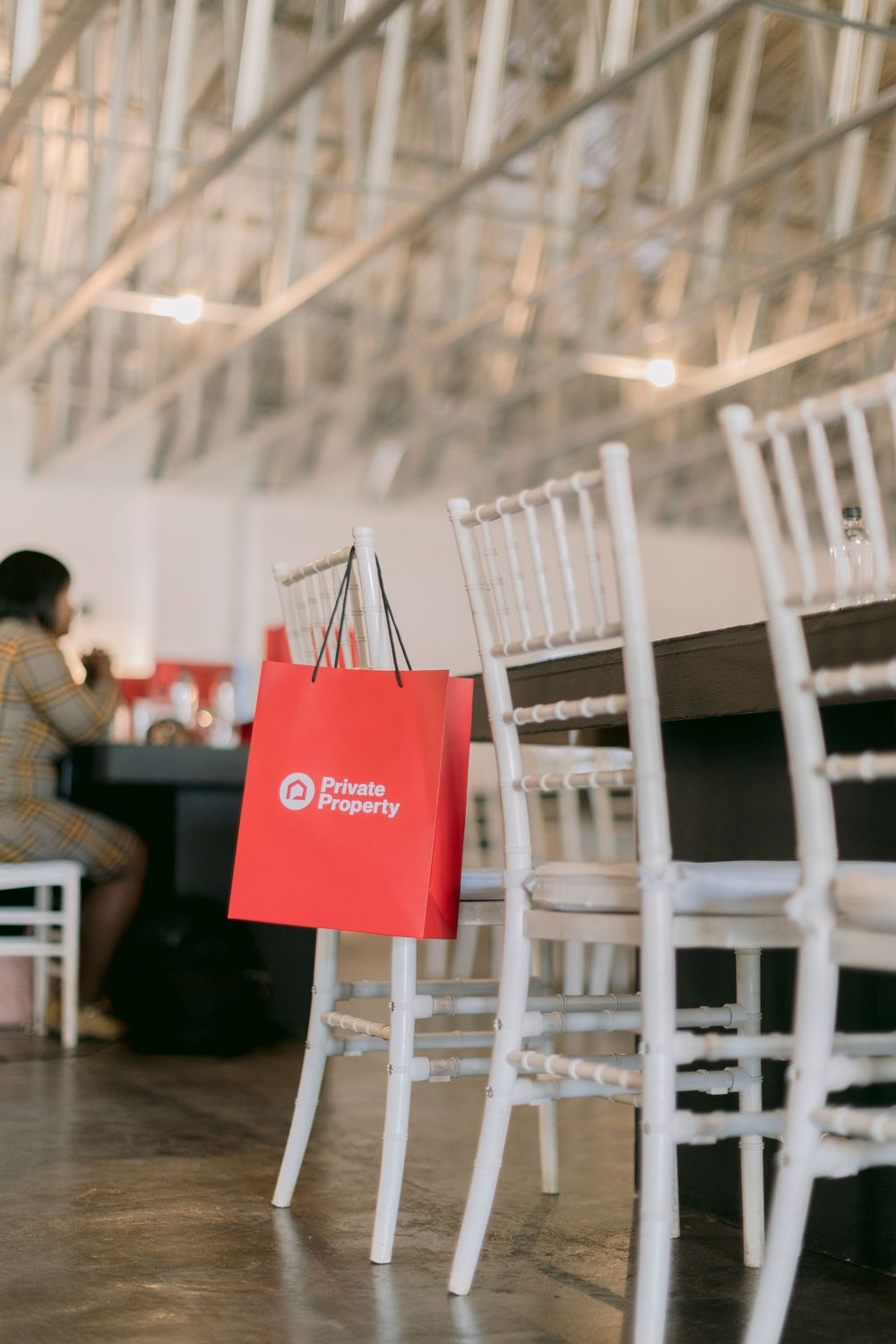 Red Private Property branded shopping bag hanging on a white chiavari chair at an event.
