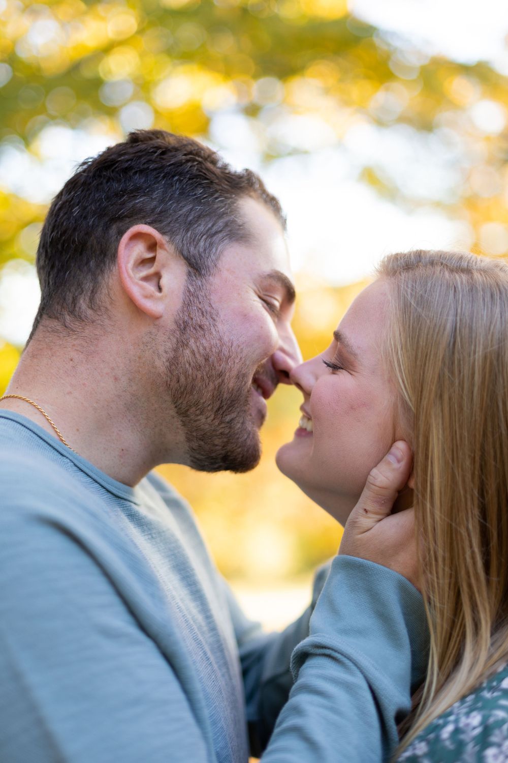 A romantic couple sharing an intimate moment outdoors with golden autumn bokeh in the background.
