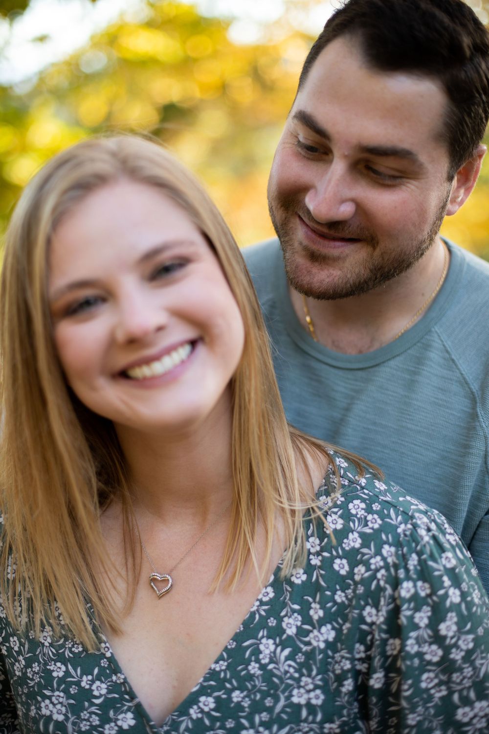 A couple smiling together during an outdoor autumn photoshoot with warm lighting.