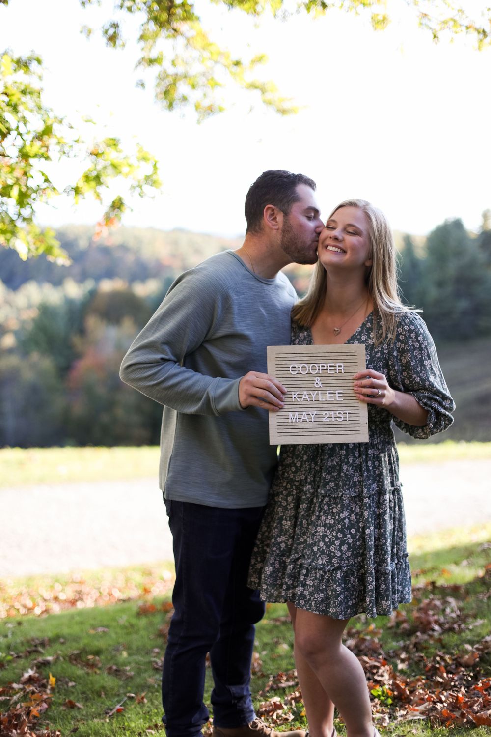 A couple shares a joyful moment while holding a sign during their engagement photoshoot.