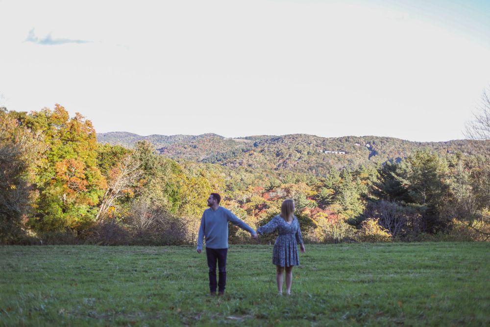 A couple stands together overlooking a scenic autumn landscape with rolling hills.