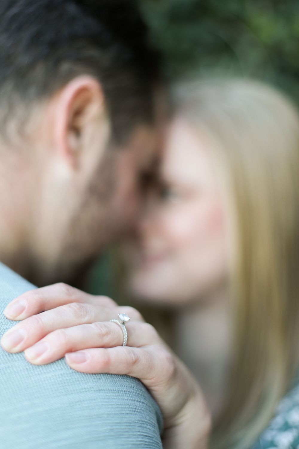 Close-up of an engagement ring being shown on a woman's hand with a blurred background.
