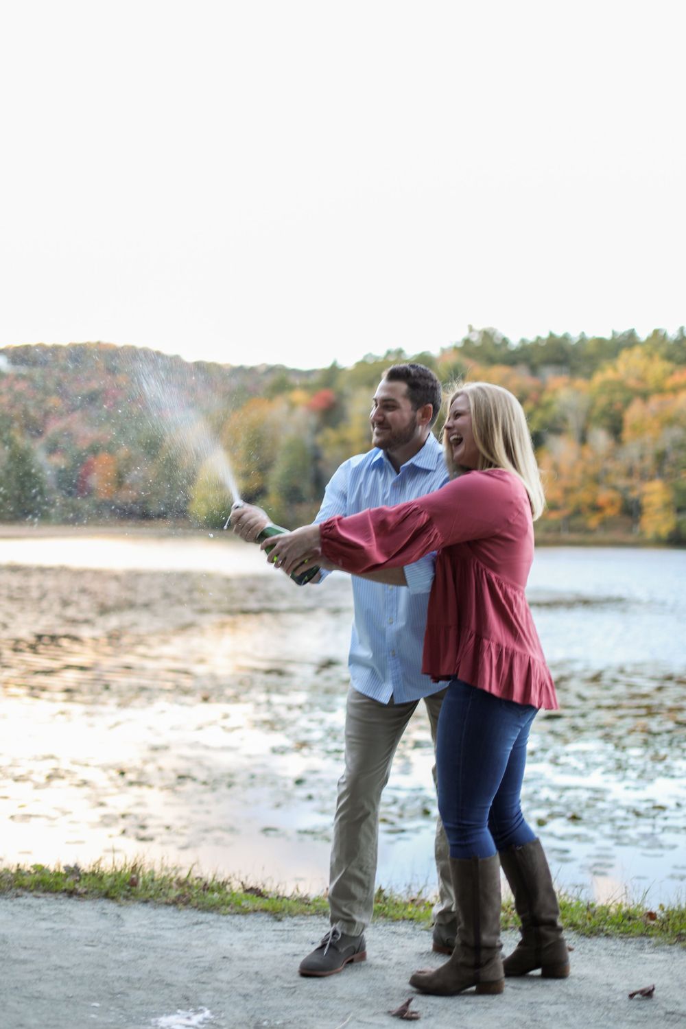 Couple playfully dancing together by a lake during autumn.