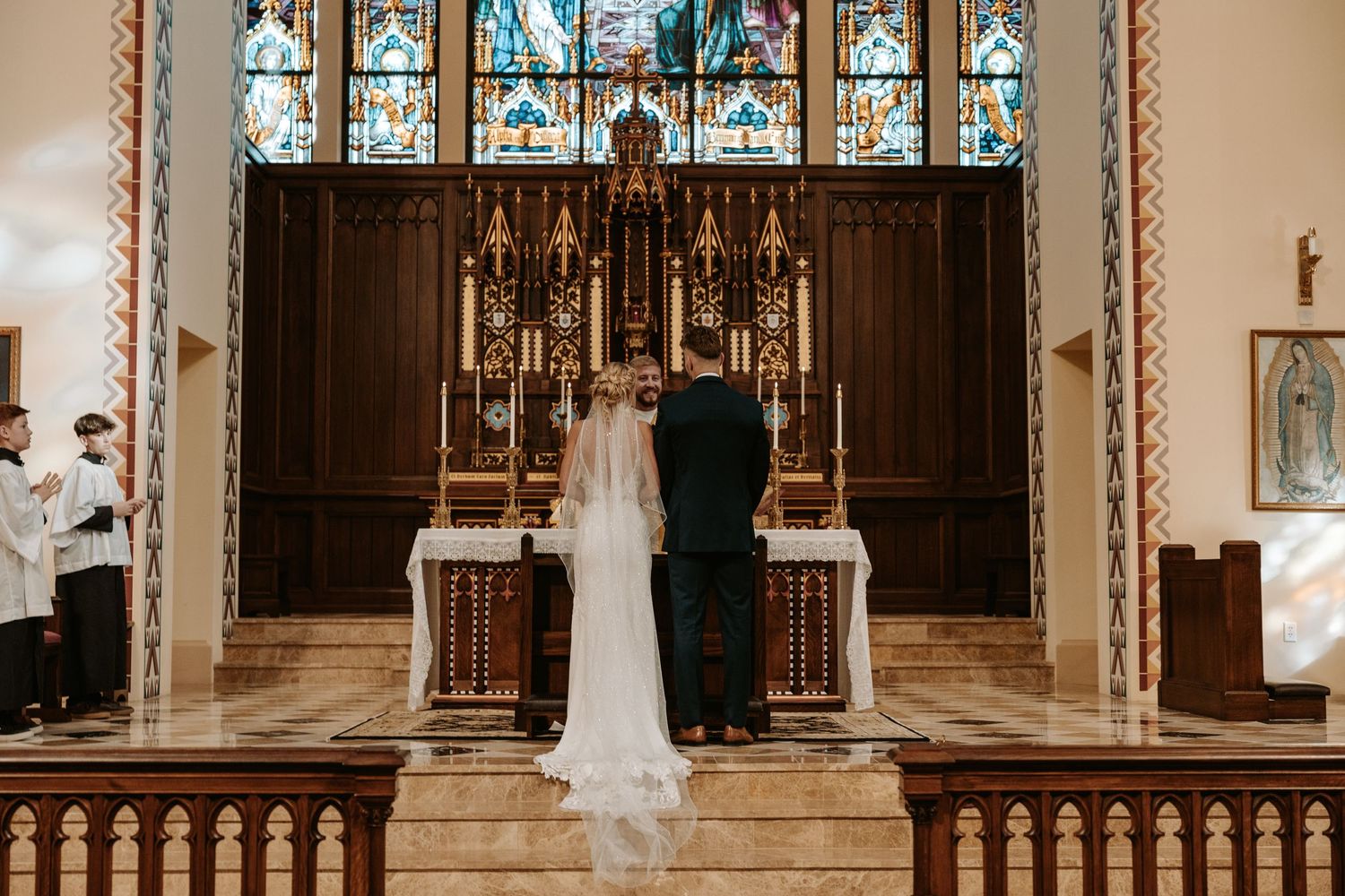 A traditional church wedding ceremony taking place at the altar with stained glass windows in the background.