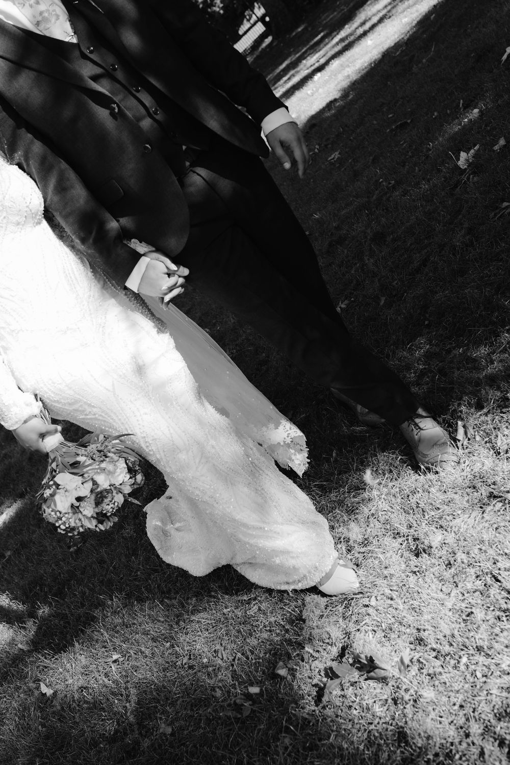 Black and white overhead shot of bride and groom holding hands while walking on grass.