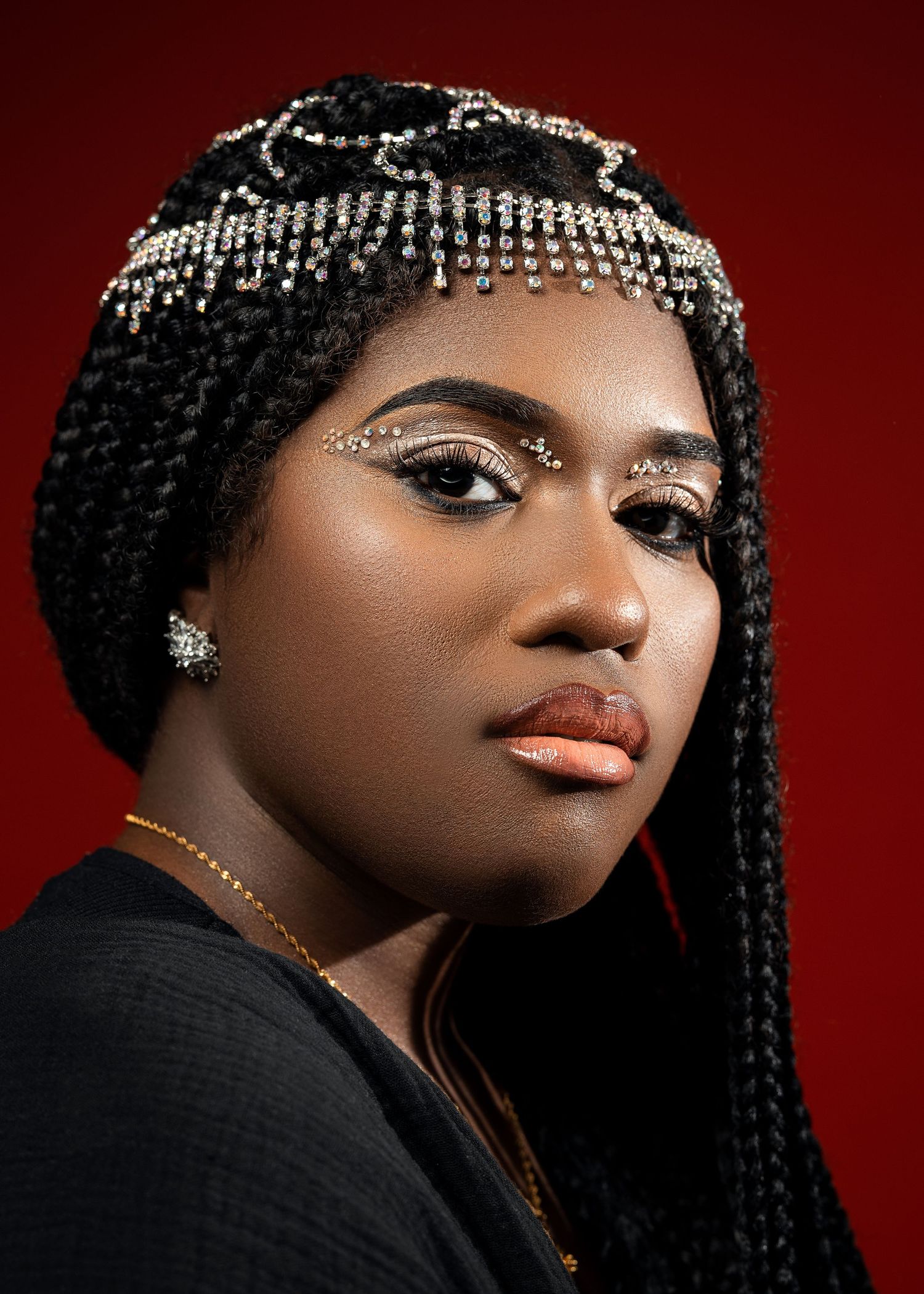 Close-up portrait with ornate beaded headpiece against red background.